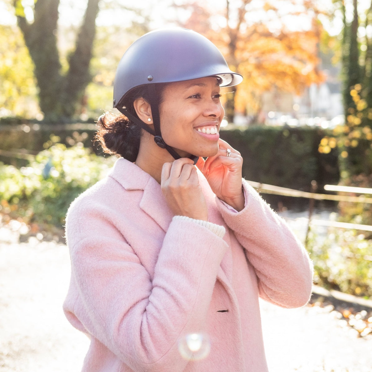 Woman in a pink coat fastening the strap of a Dashel ReCycle Navy Blue bike helmet