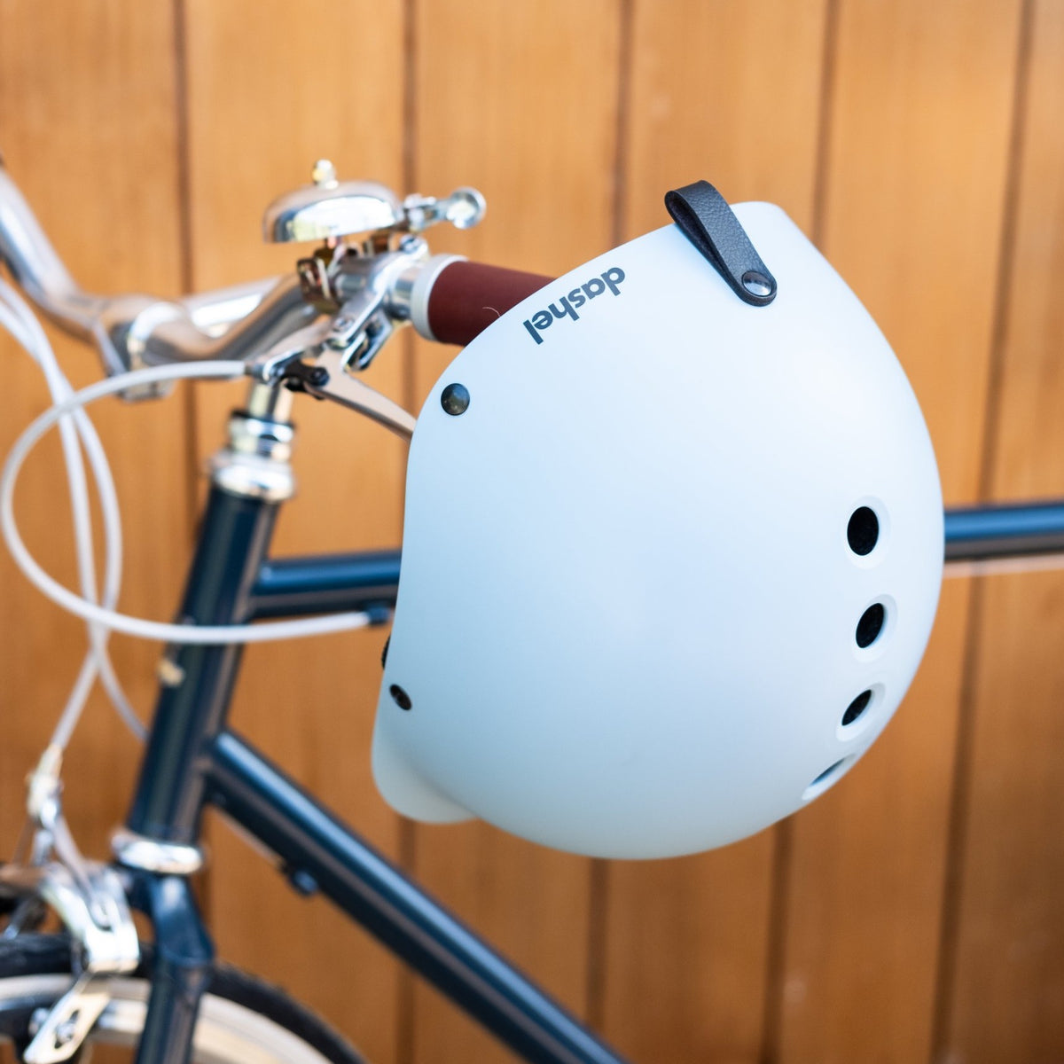 Dashel ReCycle Sky Blue bike helmet hanging from bike handlebars by its leather loop