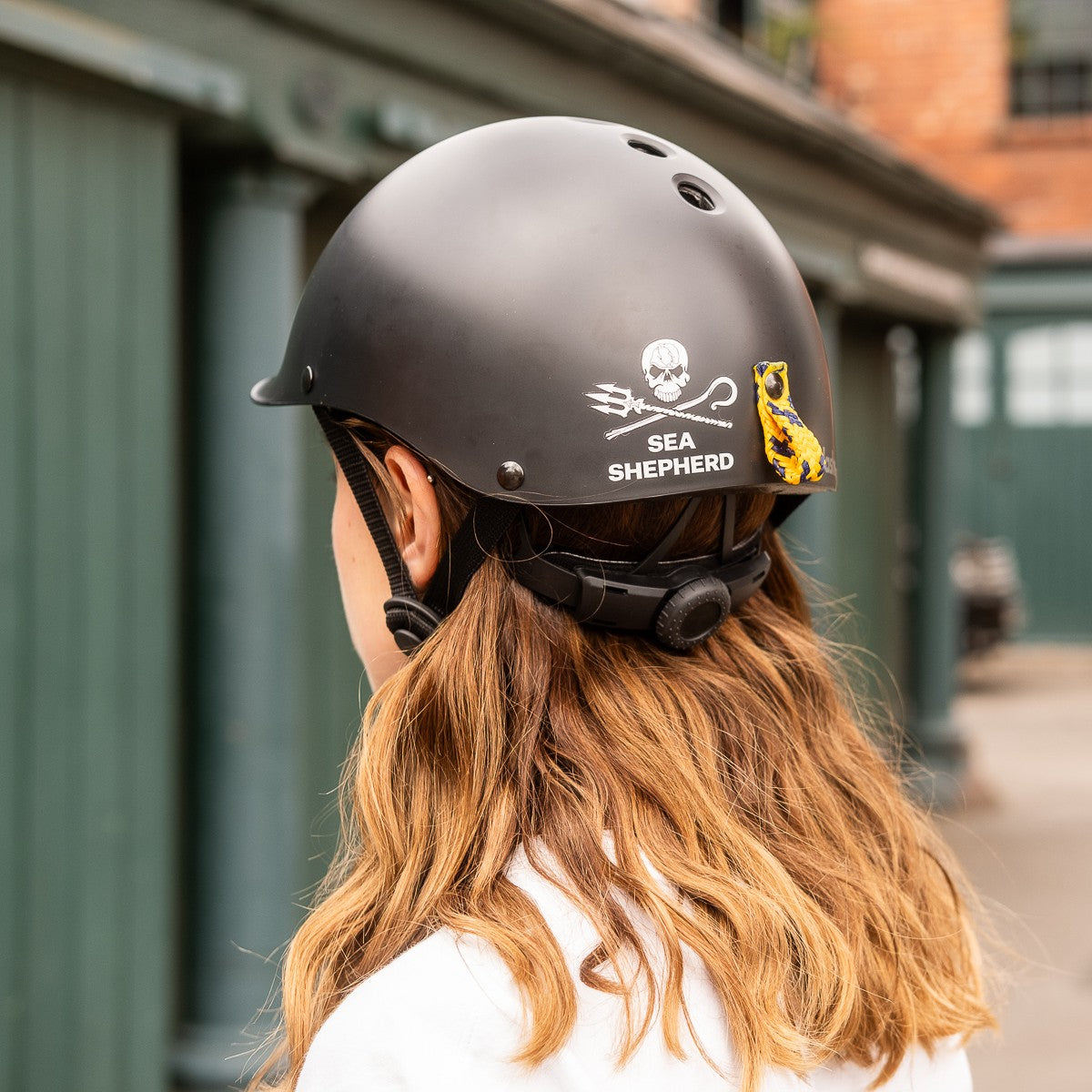 Rear view of a woman wearing the Sea Shepherd x Dashel Ocean Edition Black bike helmet showing the Sea Shepherd logo and ghost net loop